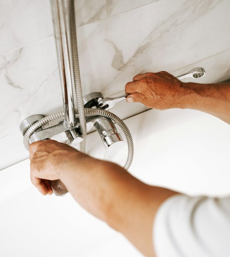 Eine Person repariert einen Wasserhahn an einer weißen Fliesenwand.